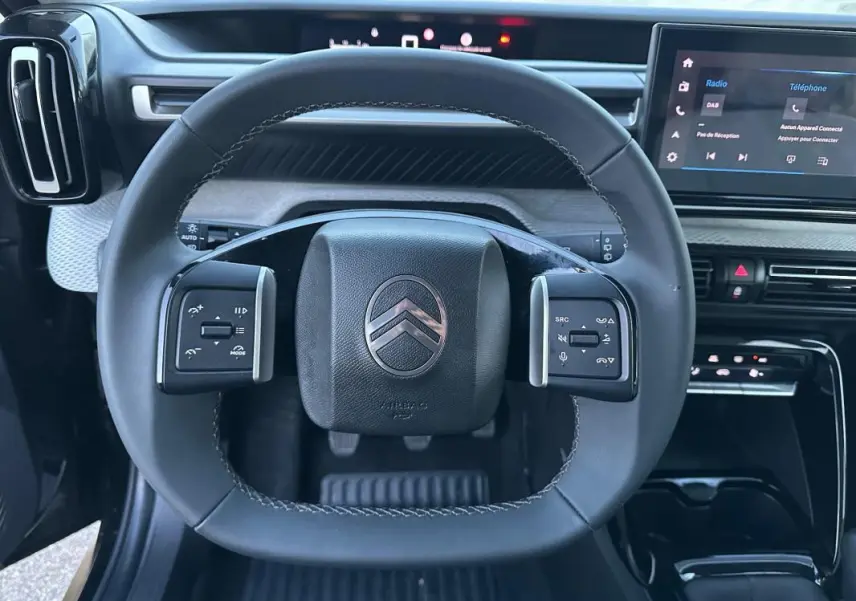 Vue rapprochée du volant noir de la Citroën C3 2025 avec commandes intégrées et tableau de bord numérique.