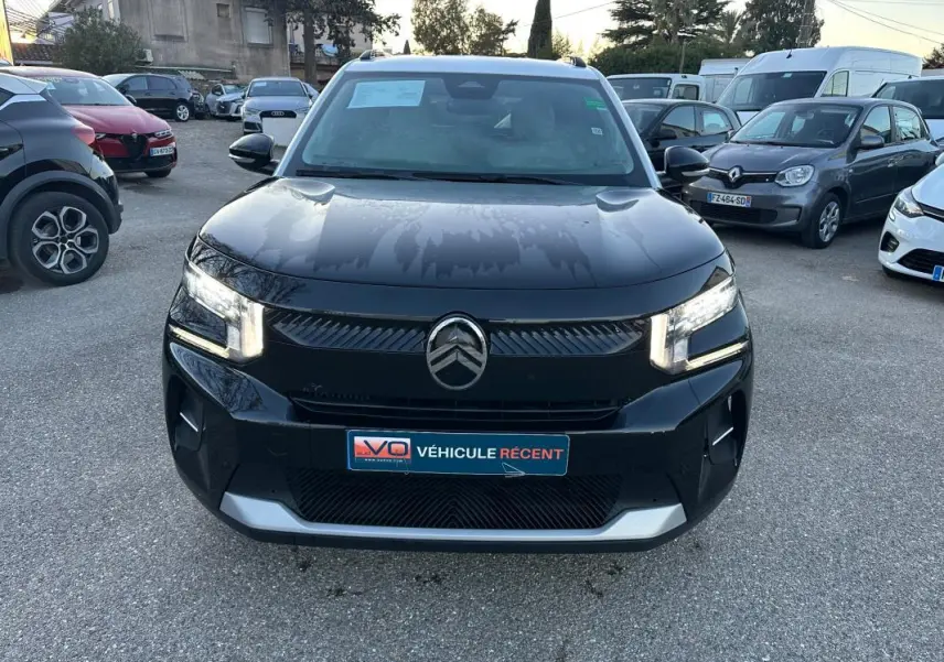 Vue avant d'une Citroën C3 noire 2025 avec phares allumés et logo Citroën bien visible sur un parking.