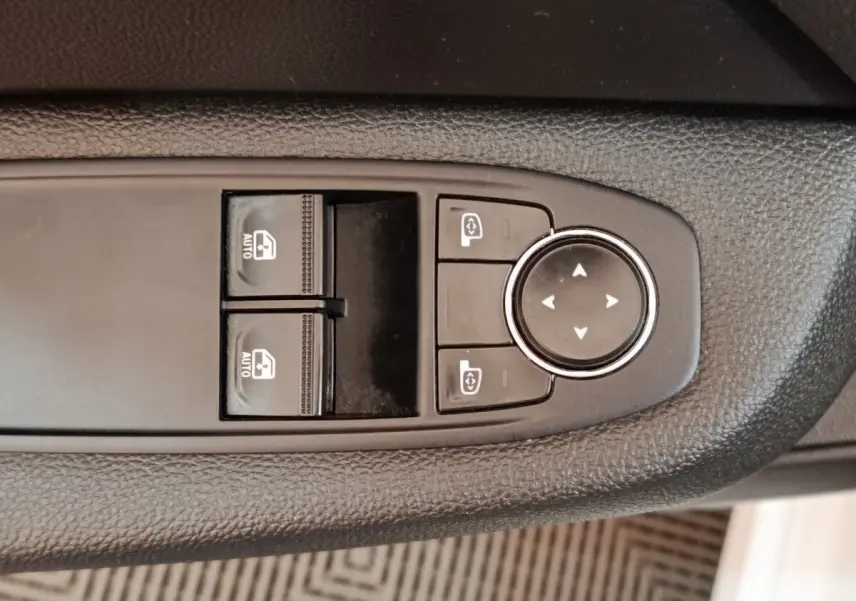 Gros plan sur les commandes de réglage des vitres et des rétroviseurs sur la porte côté conducteur d'une Renault Clio blanche.