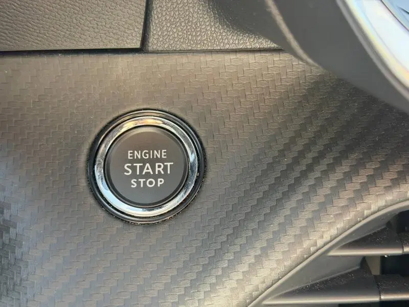 Gros plan sur le bouton start/stop moteur entouré d’un décor noir à effet carbone dans une Peugeot 2008 gris.