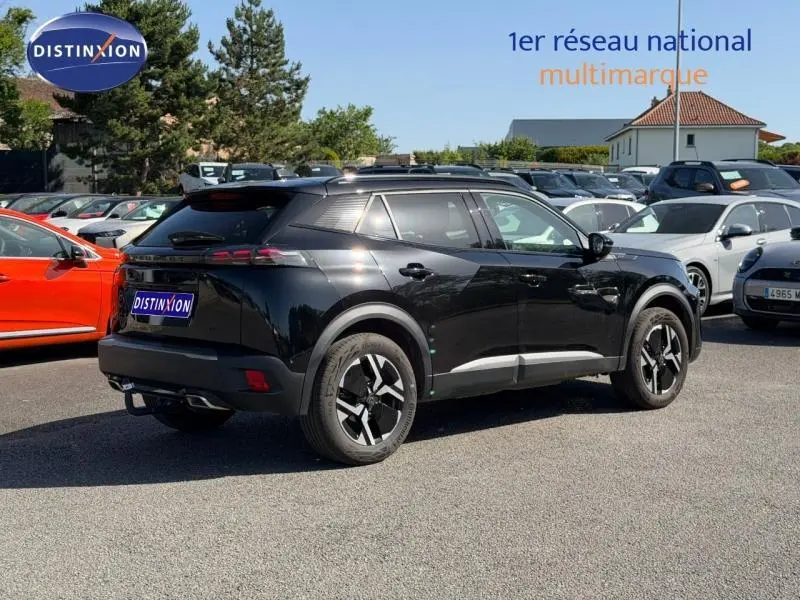 Peugeot 2008 gris 3/4 arrière droit, jantes alu noires, barres de toit et becquet arrière visibles en extérieur.