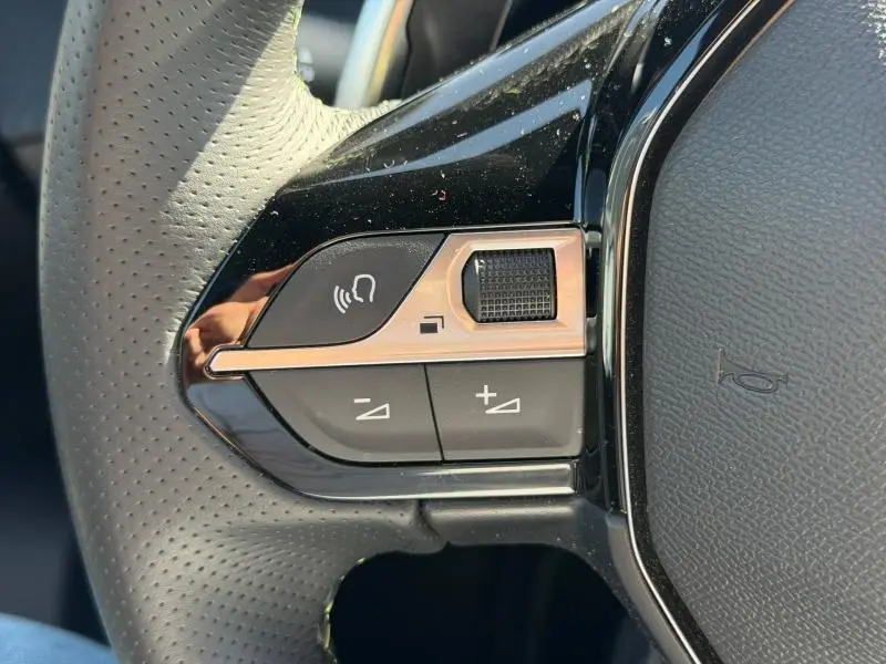 Gros plan sur les commandes gauche du volant cuir perforé du Peugeot 2008 gris, avec molette et boutons multifonctions.
