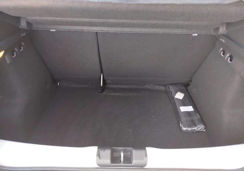 Coffre ouvert d'une Dacia Sandero Blanc Glacier, vue intérieure montrant un espace de rangement vide avec un accessoire noir posé à droite.
