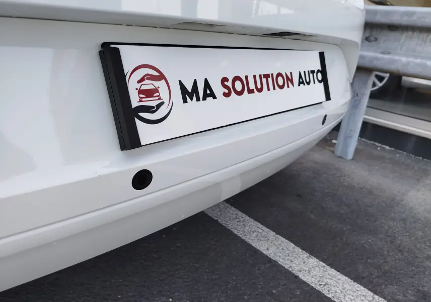 Gros plan sur le pare-chocs arrière blanc glacier de la Dacia Sandero 2025 avec capteurs de recul visibles.