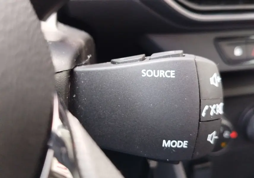 Gros plan sur la commande au volant noire avec boutons "SOURCE" et "MODE" du Dacia Sandero blanc glacier 2025.