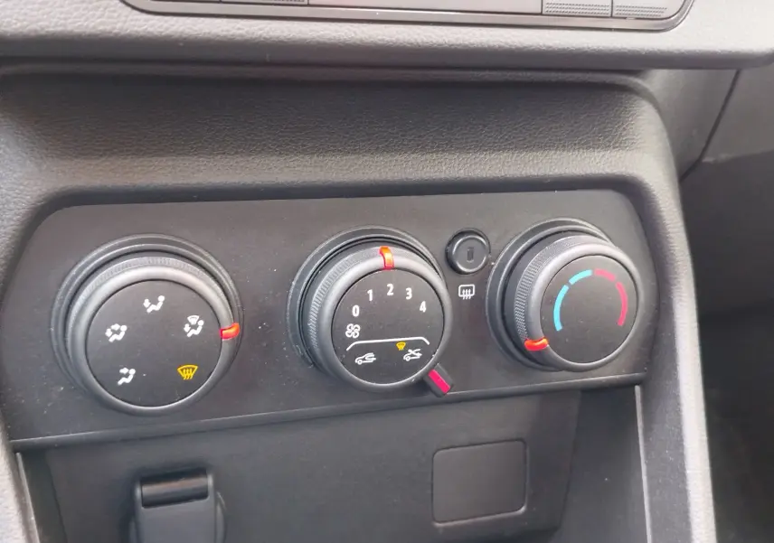 Gros plan sur les commandes de climatisation noires du tableau de bord d'une Dacia Sandero blanche, avec voyants rouges allumés.