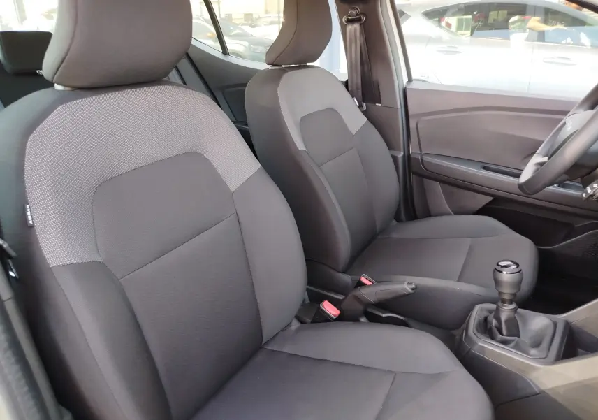 Vue intérieure côté avant droit du Dacia Sandero 2025, sièges tissu gris foncé avec console centrale et levier de vitesses manuel.