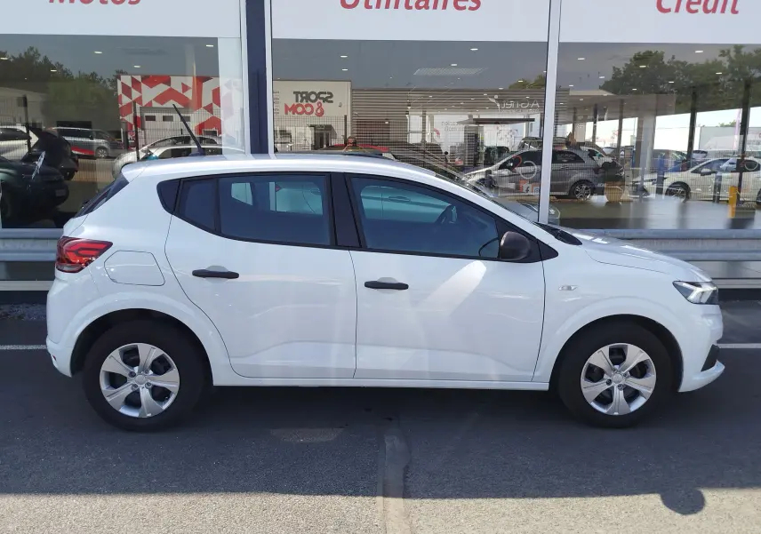 Vue de profil côté gauche d'une Dacia Sandero 2025 blanc glacier, compacte avec jantes alliage et poignées noires.