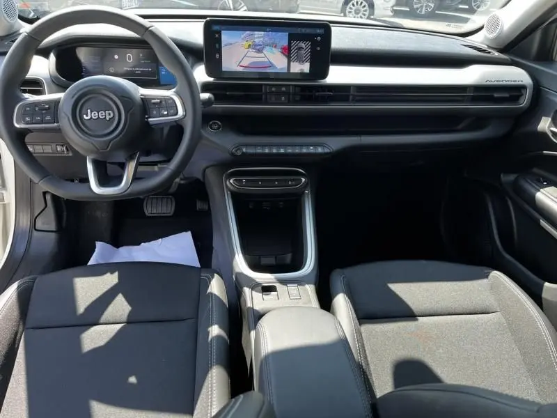 Vue intérieure avant du Jeep Avenger électrique blanc 2025, tableau de bord moderne avec écran tactile central et volant multifonction.
