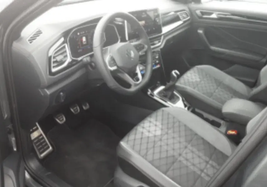 Vue intérieure côté conducteur du Volkswagen T-Roc 2025, sièges tissu gris avec surpiqûres losanges et tableau de bord digital.