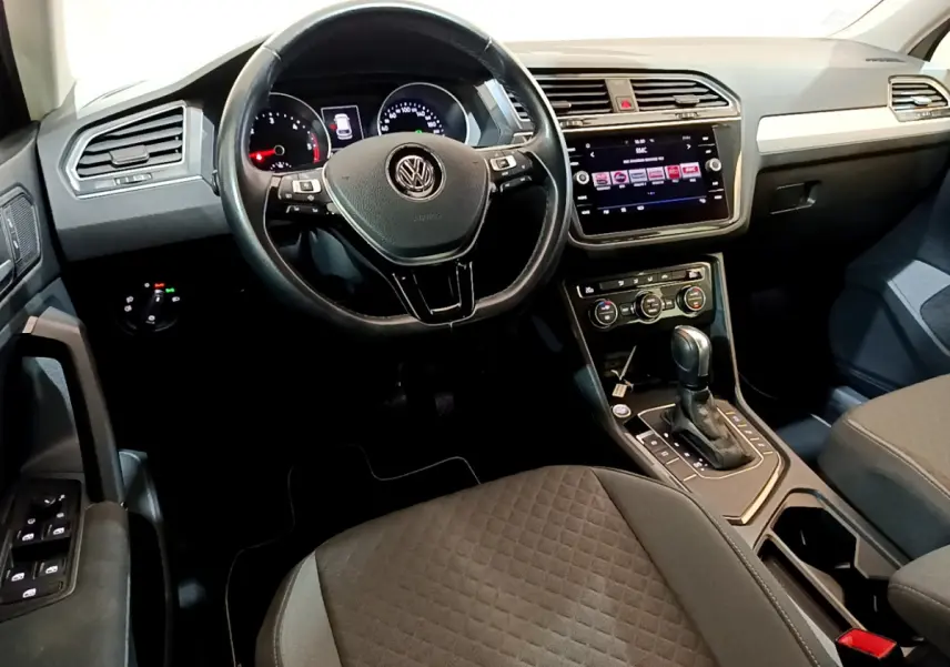 Vue intérieure avant du Volkswagen Tiguan 2020 avec tableau de bord noir, volant cuir multifonctions et écran tactile central.