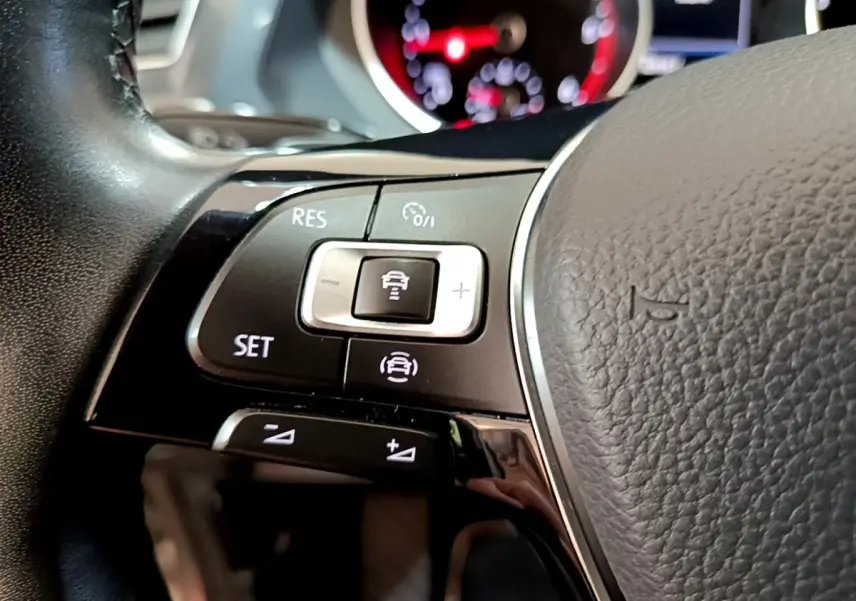 Gros plan sur les commandes du volant côté gauche du Volkswagen Tiguan gris clair, avec tableau de bord numérique en arrière-plan.