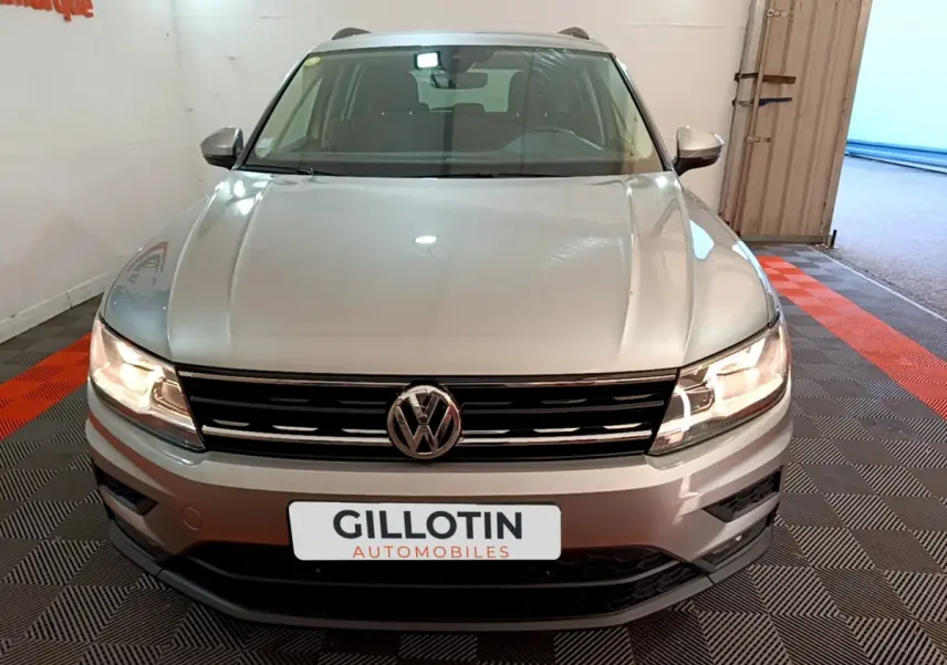 Vue frontale d'un Volkswagen Tiguan gris clair avec phares allumés et calandre noire brillante.