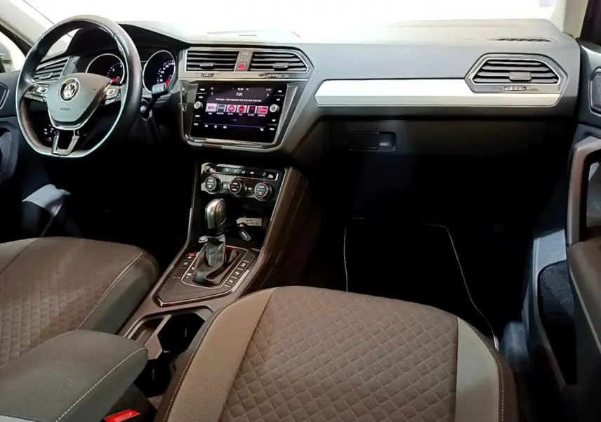 Intérieur du Volkswagen Tiguan 2020, vue du poste de conduite avec volant cuir, écran tactile et console centrale noire.