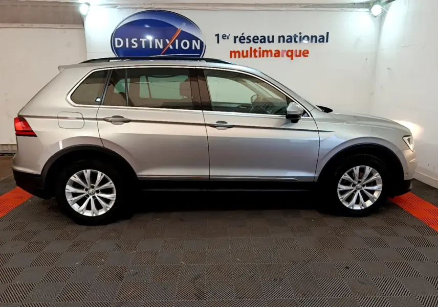 Profil côté gauche d'un Volkswagen Tiguan gris clair 2.0 TDI 150 DSG7 Confortline Business de 2020 en intérieur showroom.