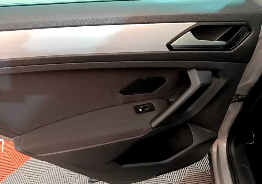 Vue rapprochée de la porte avant droite du Volkswagen Tiguan gris clair, avec poignée et commande de verrouillage intégrées.