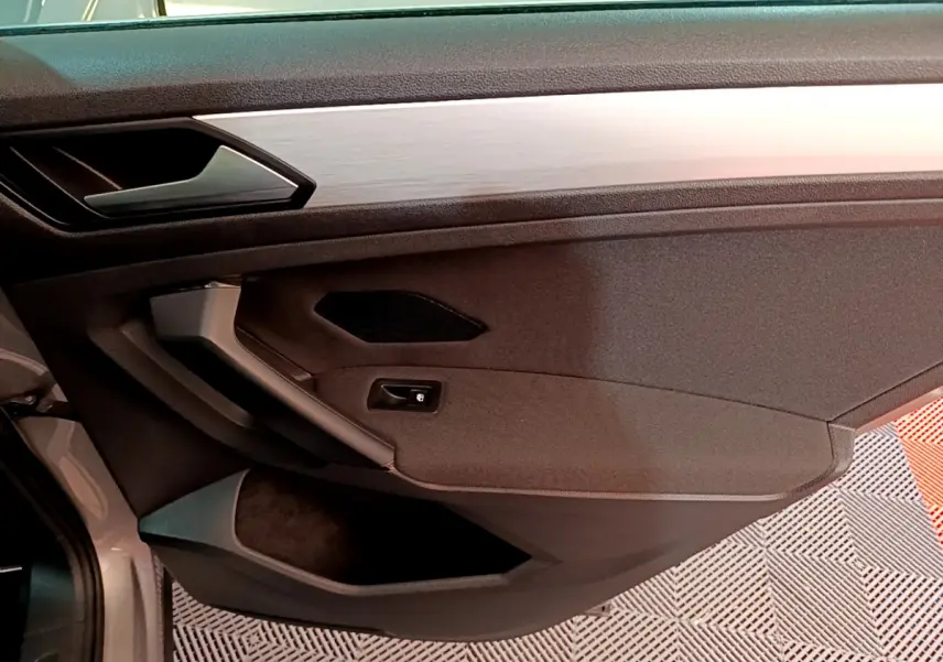 Vue intérieure du panneau de porte côté gauche du Volkswagen Tiguan gris clair, avec poignée argentée et haut-parleur intégré.
