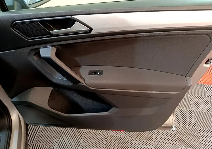 Vue rapprochée de la porte côté gauche du Volkswagen Tiguan gris clair, avec poignée et panneau noir mat.