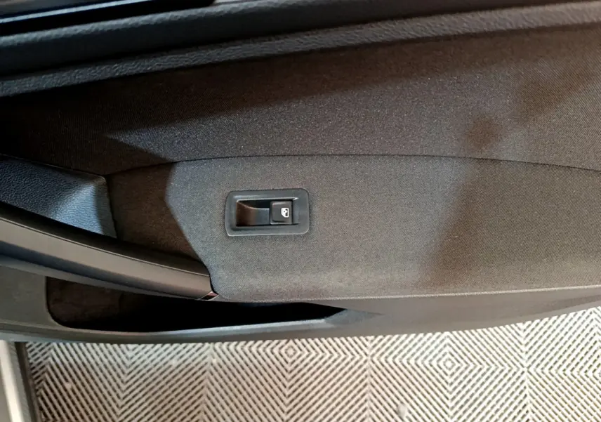 Gros plan sur le bouton de verrouillage de porte intégré dans le panneau de porte noir du Volkswagen Tiguan gris clair.