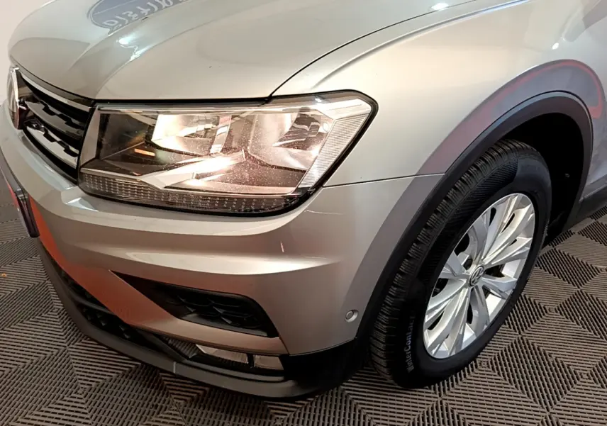 Gros plan sur l'avant droit gris clair du Volkswagen Tiguan 2.0 TDI 150 avec phare allumé et jante alu visible.