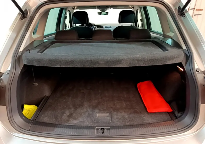 Coffre ouvert d'un Volkswagen Tiguan gris clair 2020, vue arrière avec cache-bagages et objets rouge et jaune visibles.
