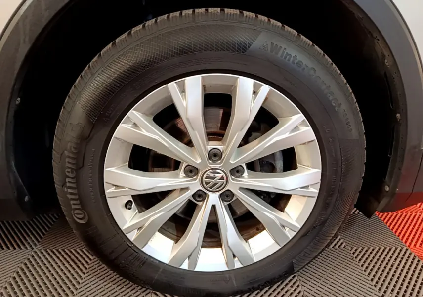 Gros plan sur la roue avant droite du Volkswagen Tiguan gris clair avec jante alliage et logo VW central.
