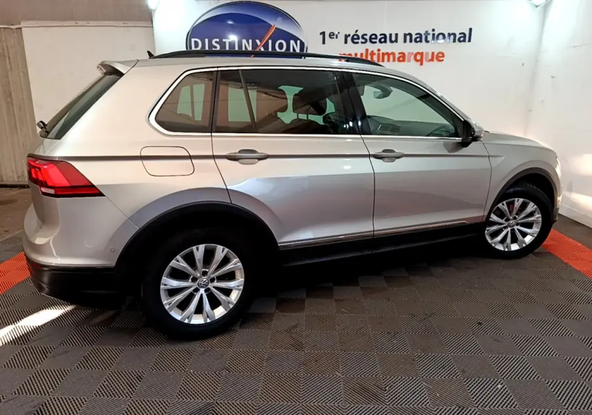 Profil droit d'un Volkswagen Tiguan gris clair 2020 avec jantes alliage et barres de toit noires dans un showroom