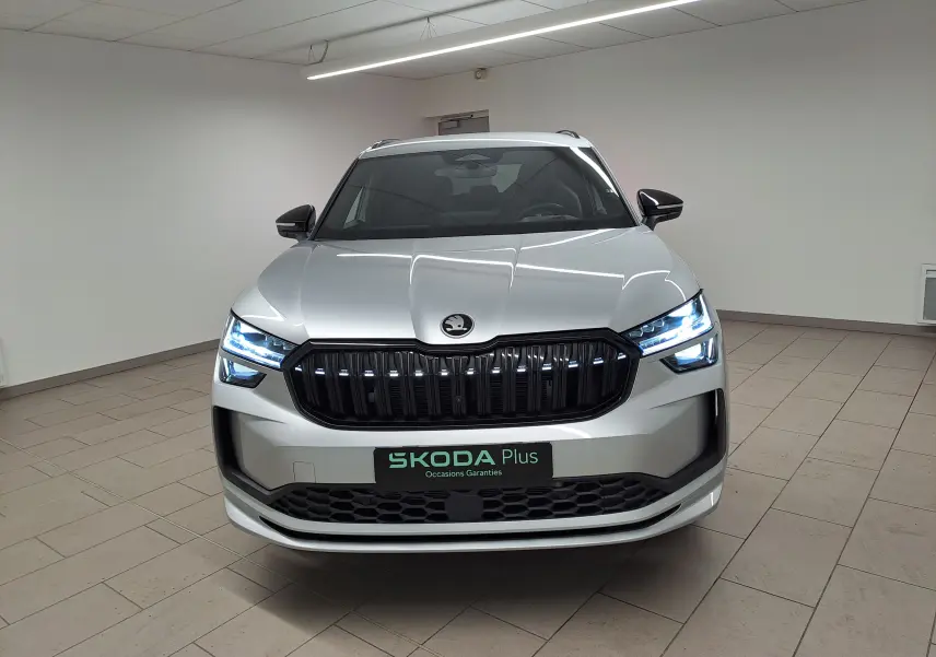 Vue frontale d'un Skoda Kodiaq gris argent 2025 avec calandre noire et phares LED allumés en intérieur.