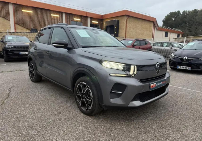 Vue 3/4 avant d'une Citroën C3 gris métallisé avec jantes alliage 17 pouces et barres de toit visibles.