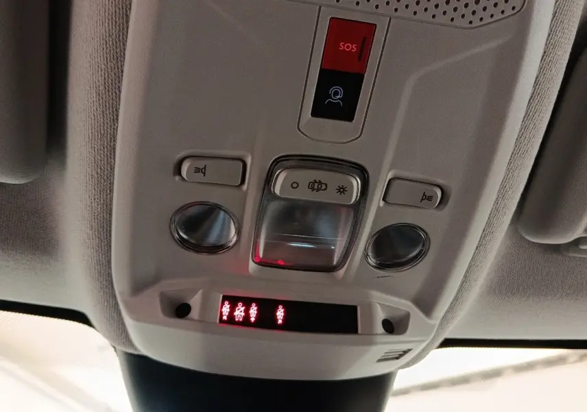 Gros plan sur la console de plafonnier gris clair avec boutons d’éclairage et indicateurs de ceinture allumés dans une Citroën C4 gris foncé.
