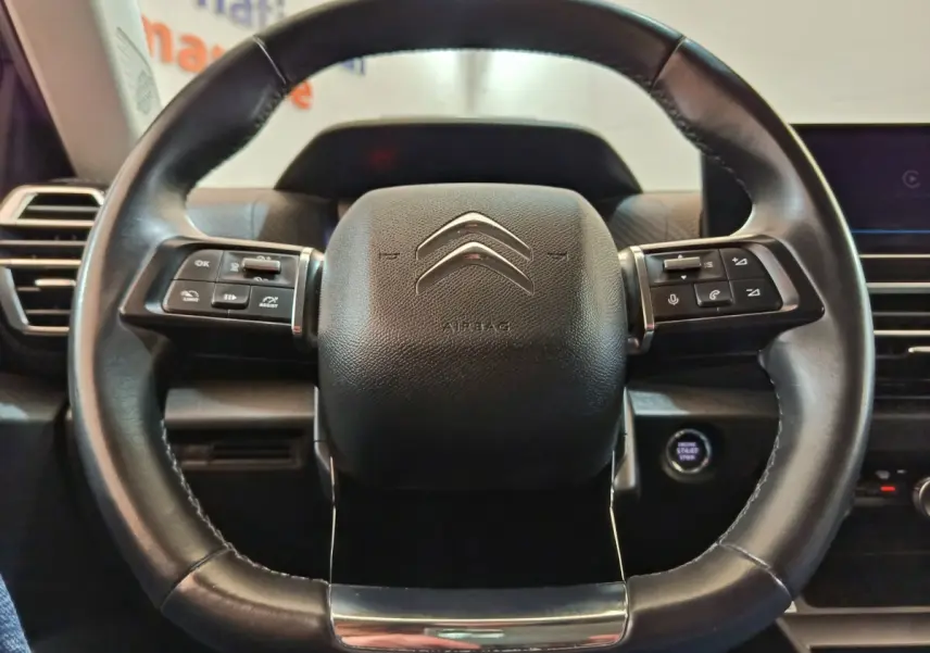 Gros plan sur le volant cuir noir du Citroën C4 2022 avec commandes multifonctions et bouton démarrage visible à droite.