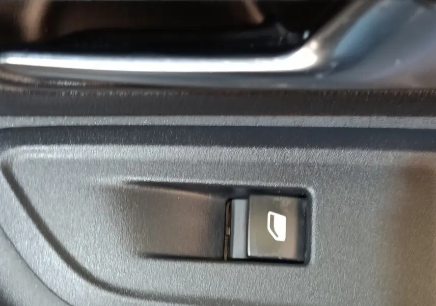 Gros plan sur le bouton de commande de lève-vitre côté conducteur d'une Citroën C4 gris foncé.