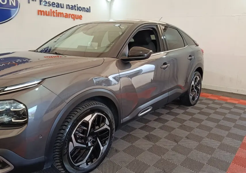 Vue 3/4 avant droit d'une Citroën C4 gris foncé avec jantes noires et détails chromés, stationnée en intérieur.