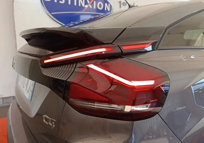 Feu arrière allumé en gros plan côté gauche d'une Citroën C4 gris foncé, avec aileron et logo visible.
