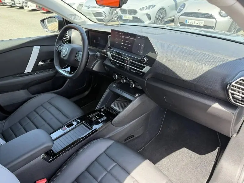 Vue intérieure côté conducteur de la Citroën C4 1.2 Hybride 145ch avec tableau de bord moderne et sièges noirs en tissu enduit.