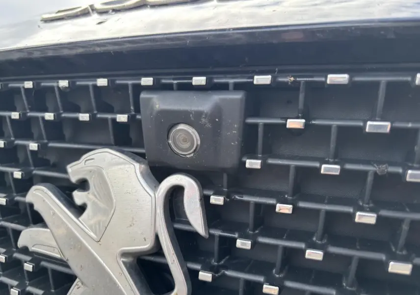 Gros plan sur la calandre noire du Peugeot 3008 2022, avec logo lion argenté et caméra frontale intégrée.