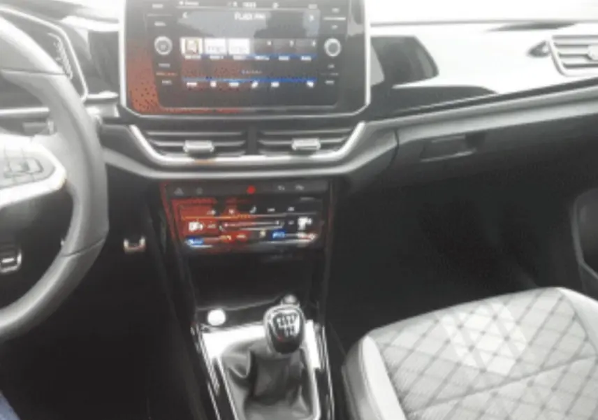 Vue intérieure centrée sur la console centrale du Volkswagen T-Roc gris platinium avec levier de vitesse manuel et écran tactile.