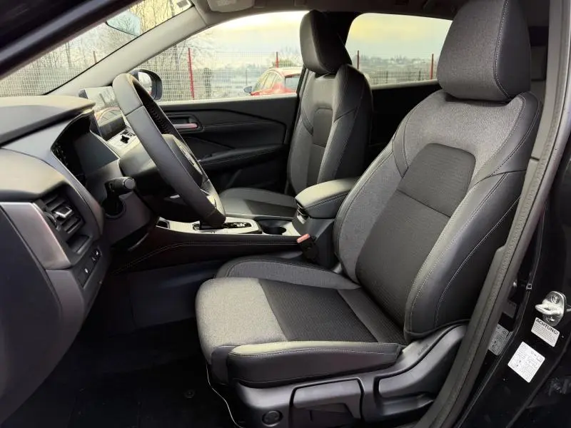 Vue intérieure côté conducteur du Nissan Qashqai Hybrid e-POWER 2025, sièges tissu gris et tableau de bord moderne.
