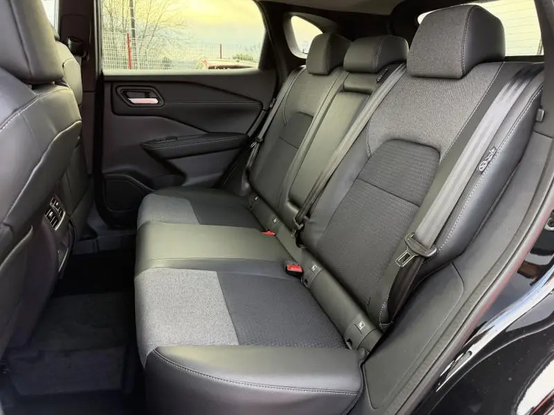 Vue latérale droite de l’intérieur arrière du Nissan Qashqai Hybrid e-POWER 2025, sièges bi-matière gris et noir avec ceintures de sécurité.