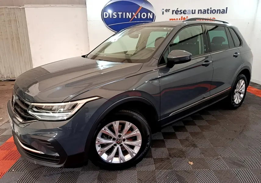 Volkswagen Tiguan gris clair vu en 3/4 avant droit dans un showroom avec jantes alliage et phares LED.