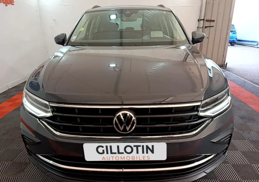 Vue frontale d'un Volkswagen Tiguan gris clair avec calandre chromée et phares LED allumés en intérieur showroom.