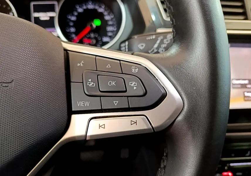 Gros plan sur les commandes gauche du volant cuir du Volkswagen Tiguan gris clair, avec tableau de bord flou en arrière-plan.