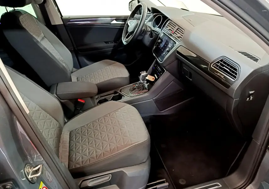 Intérieur avant du Volkswagen Tiguan gris clair, vue côté conducteur montrant sièges tissu et tableau de bord moderne.