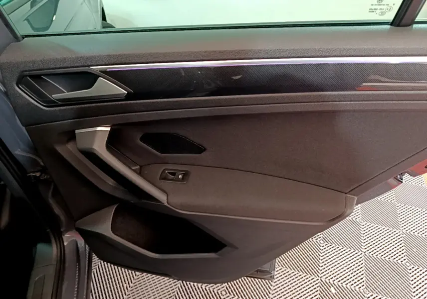Vue intérieure côté gauche de la porte avant gris clair du Volkswagen Tiguan avec poignée argentée et garniture noire.