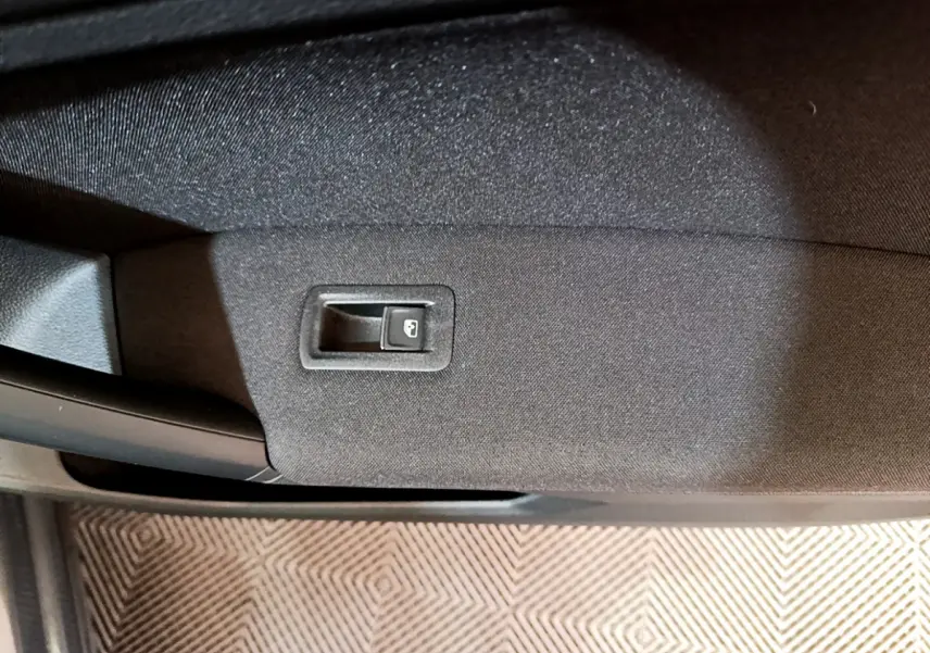 Gros plan sur le bouton d'ouverture de coffre intégré à la garniture intérieure d'une Volkswagen Tiguan gris clair.