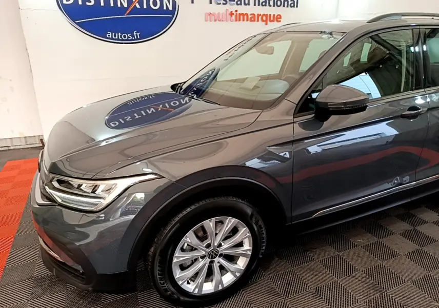 Vue 3/4 avant droit d'un Volkswagen Tiguan gris clair avec jantes alliage et phares LED dans un showroom.
