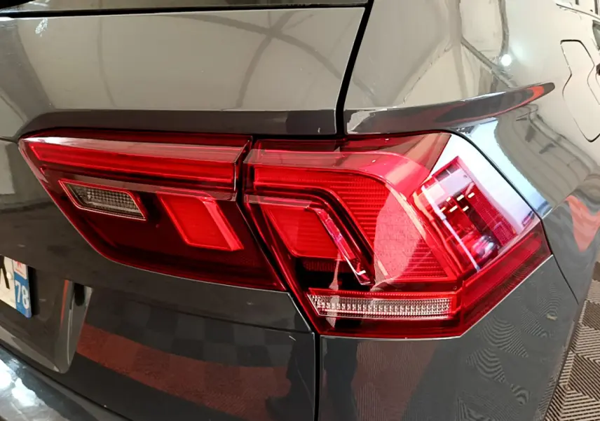 Gros plan sur le feu arrière droit rouge d'un Volkswagen Tiguan gris clair 2021, avec reflet sur la carrosserie lisse.