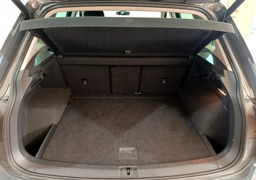 Coffre ouvert vu de l'arrière d'un Volkswagen Tiguan gris clair, espace de chargement vide et tapis noir.