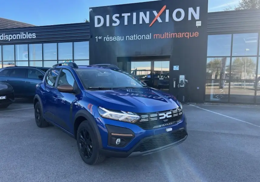 Dacia Sandero III Stepway bleu Iron en 3/4 avant droit, avec calandre noire et barres de toit brun cuivré.