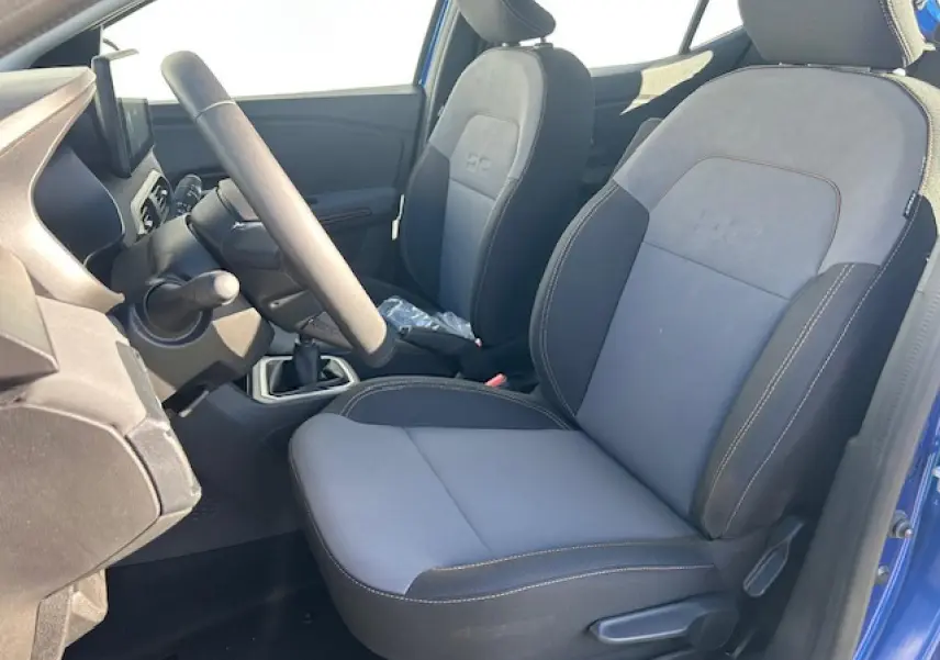 Vue intérieure côté conducteur de la Dacia Sandero III Stepway bleu Iron, sièges tissu gris avec logo DC brodé.